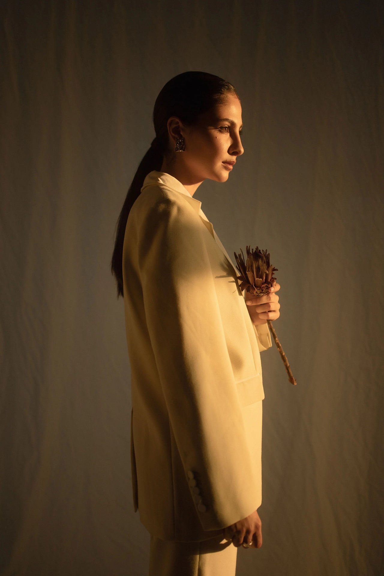Woman holding botanical in white coat with sun hitting moisturized skin